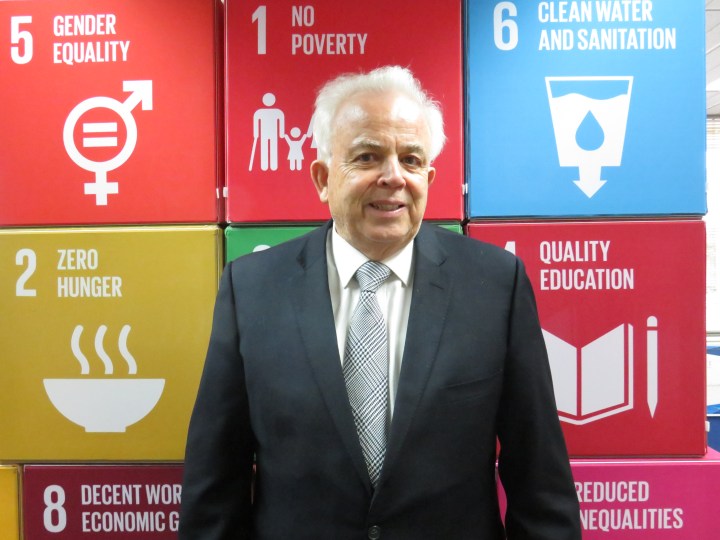 David Templeman stands in front of a board containing info graphics for some of the Sustainable Development Goals.